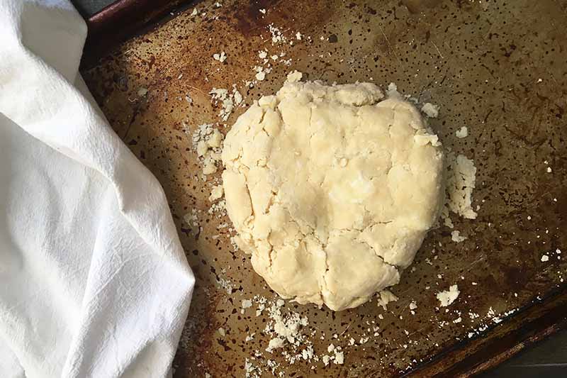 Horizontal image of pie dough on a sheet pan next to a white towel.