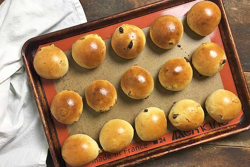 Horizontal image of baked and shiny rolls on a sheet pan lined with a silicone mat.