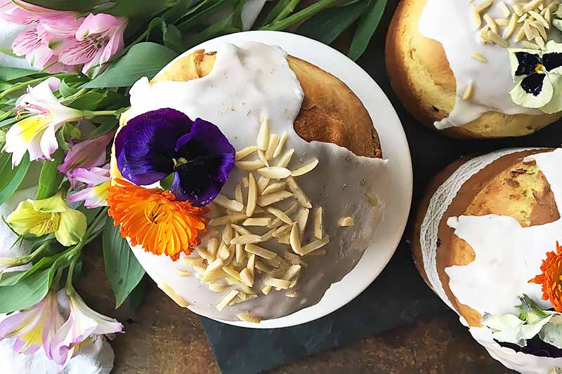 Horizontal image baked loaves topped with thick white icing and flowers next to more flowers.
