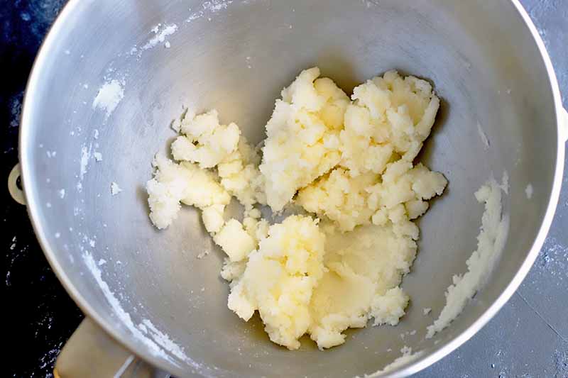 Creamed butter and granulated sugar is at the bottom of a stainless steel bowl, on a gray background.
