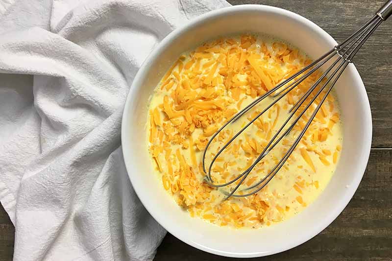 Horizontal image of an egg and cheese mixture in a bowl with a whisk.