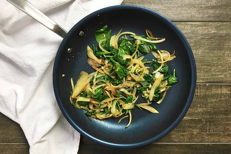 Horizontal image of a pan with a mixture of sauteed spinach and onions.
