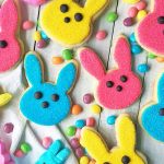 Horizontal image of assorted colored rabbit cut-out cookies on a white table with jelly beans.