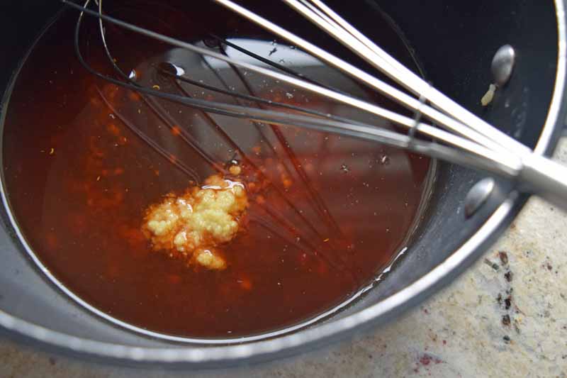 Chicken broth, soy sauce, chili garlic sauce, rice vinegar, honey, and ginger in a sauce pan being whisked together.