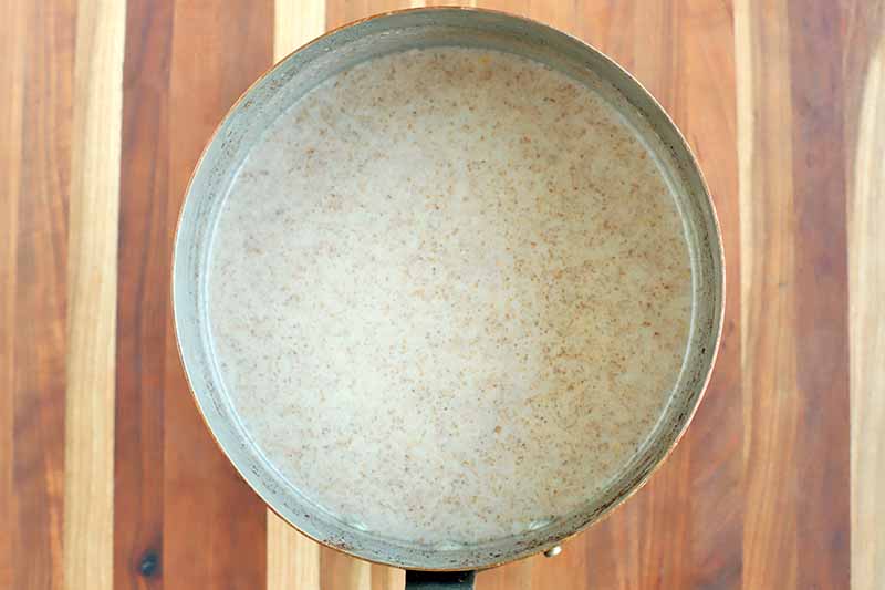 Overhead shot of a saucepan of a coconut milk mixture, on a striped wood surface.