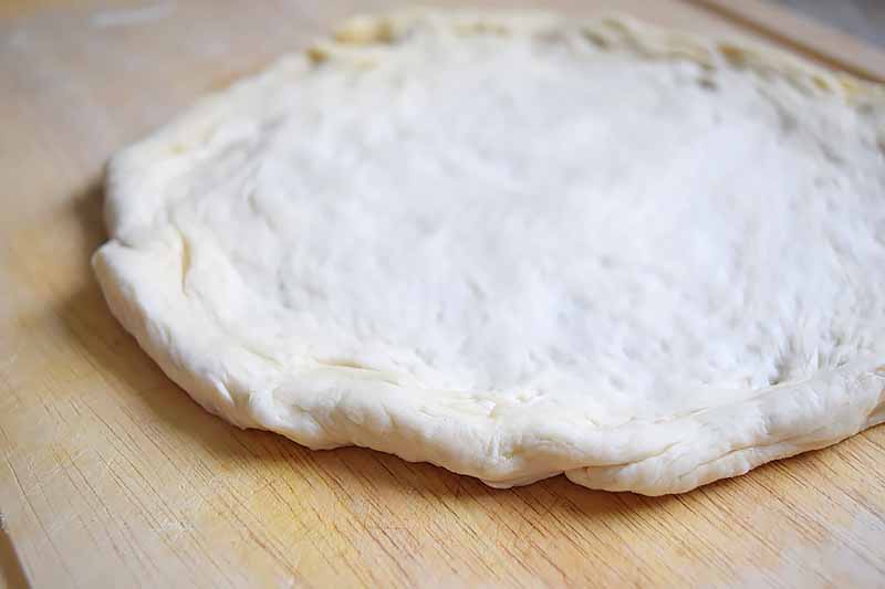 Horizontal image of a rounded flattened portion of pizza dough.