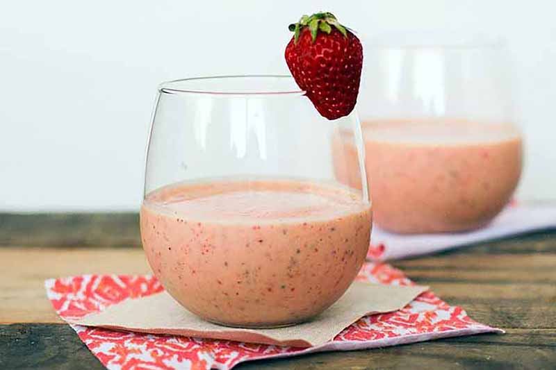 Horizontal image of pink smoothies in glasses with a strawberry garnish.