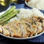 Horizontal image of a white plate with sliced and marinated grilled chicken with fresh asparagus and white rice.