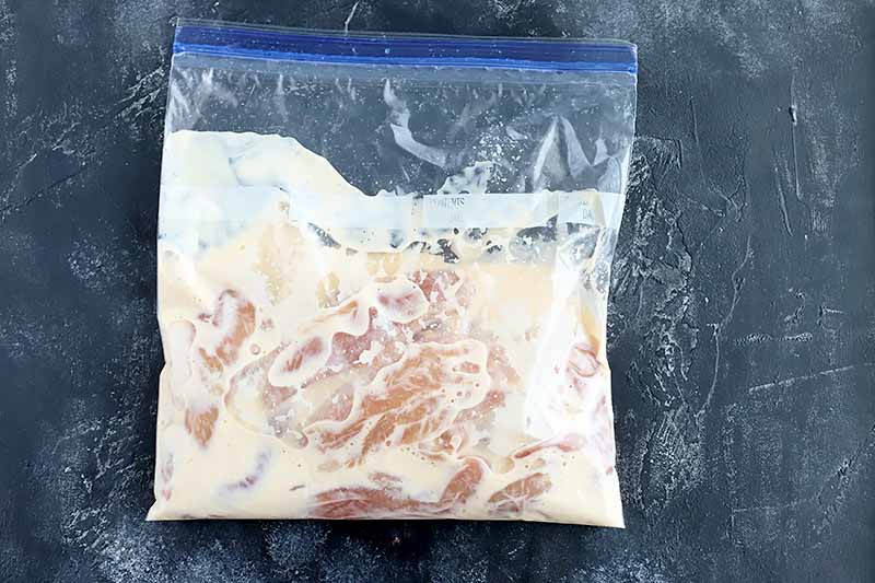 Horizontal image of an airtight bag with raw chicken and marinade on a dark surface.