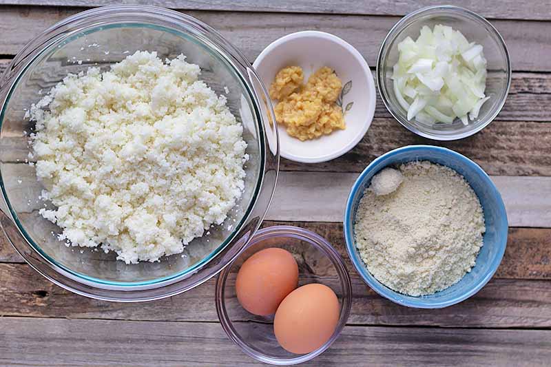 Horizontal image of ingredients for a cauliflower pizza crust on a wooden surface.