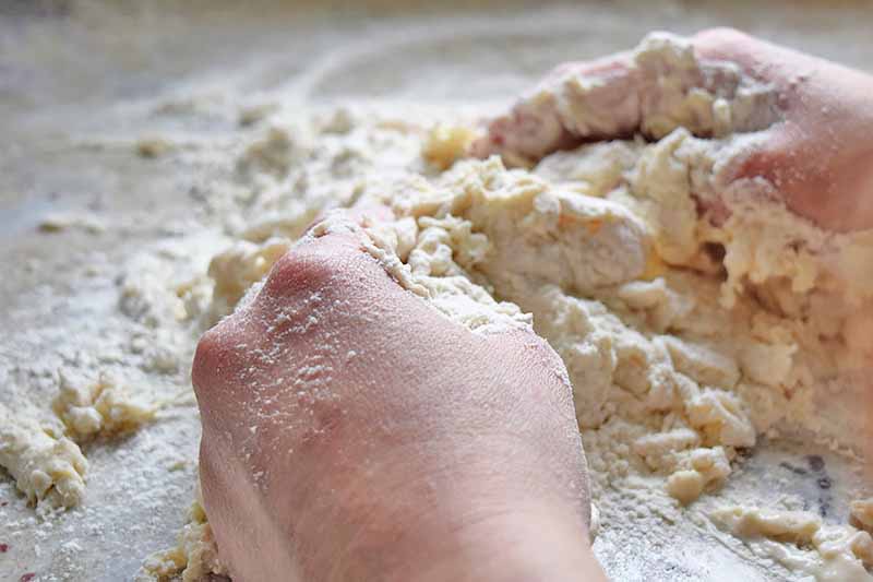 Horizontal image of a hand kneading together a dough.