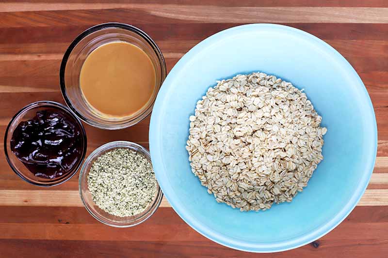Horizontal image of a big blue bowl with oats and other bowls with assorted ingredients on a wooden surface.
