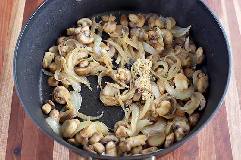 Horizontal image of a pot with cooked mushrooms and onions.