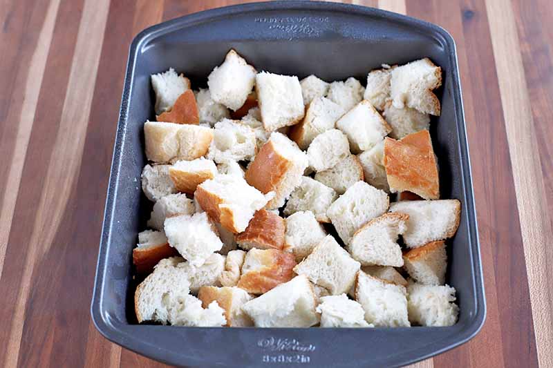Horizontal overhead image of a rectangular metal baking pan filled with cubed bread.
