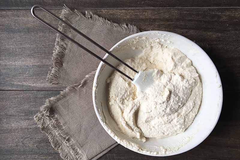 Horizontal image of a whipped ricotta mixture in a white bowl with a spatula on two tan napkins.
