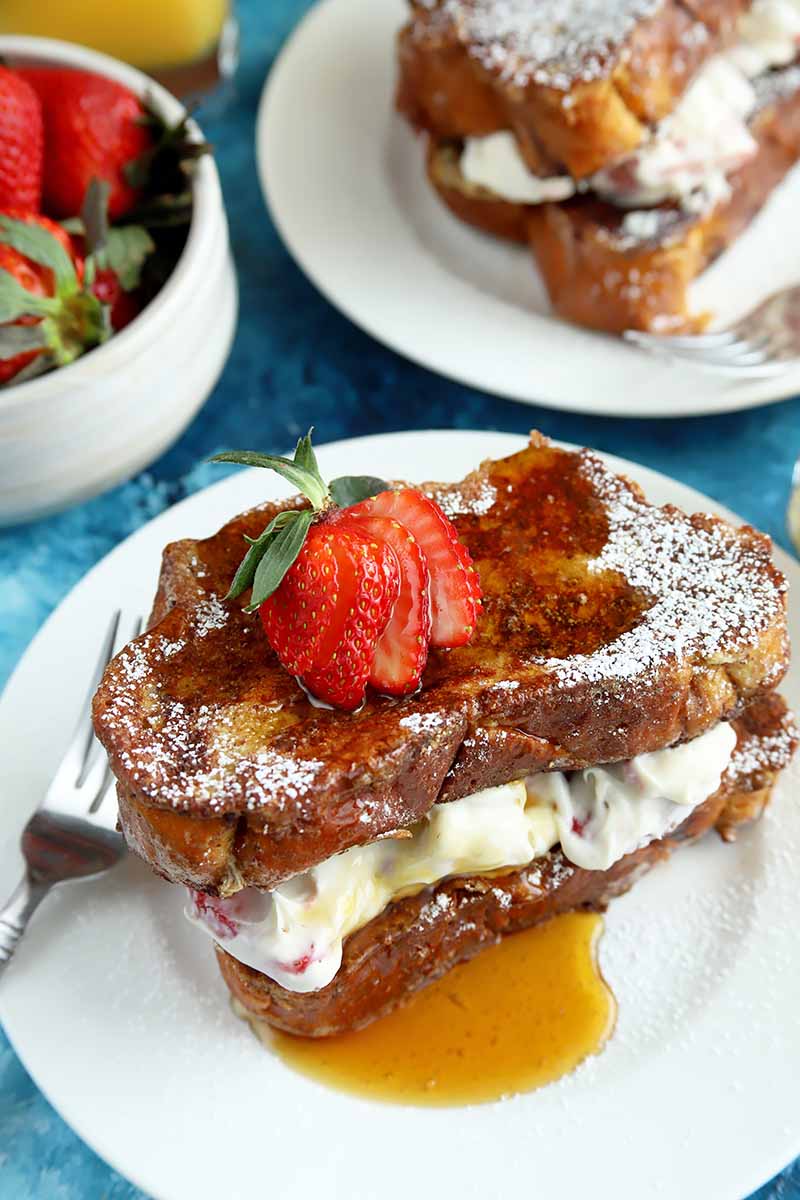 Vertical image of two white plates with stuffed French toast and syrup.