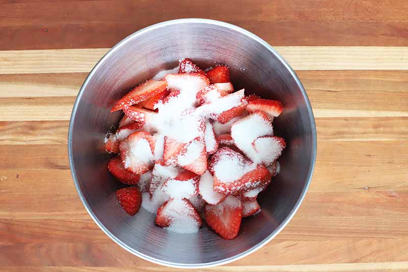 Horizontal image of a metal bowl with strawberries and granulated sugar.