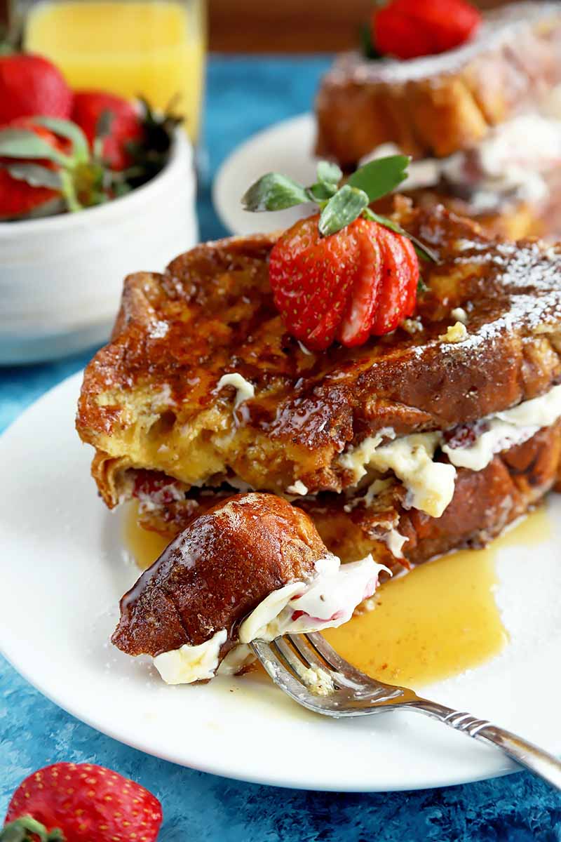 Vertical image of stacked French toast with syrup and a fork with a piece of it on a white plate.