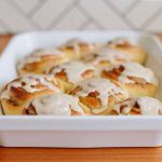 Horizontal image of a white tray with freshly baked cinnamon rolls with glaze.
