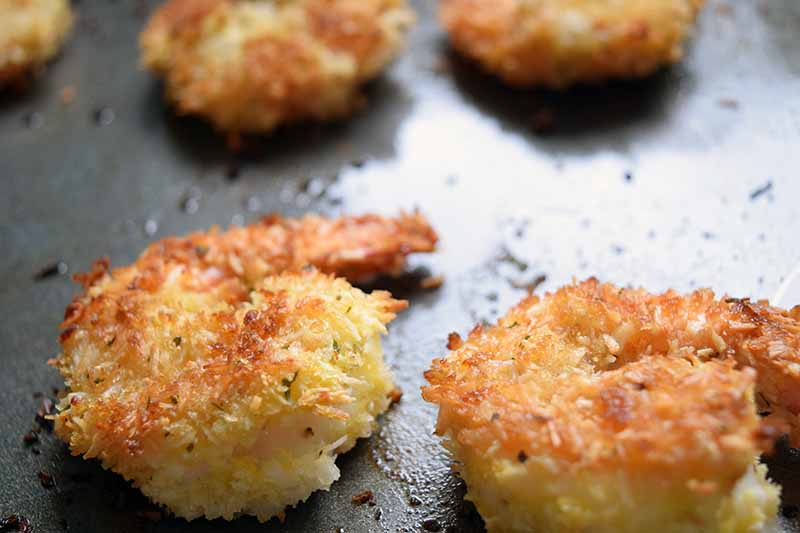 Baked shrimp with the tails on, with a coconut and panko breadcrumb crust, on a metal baking sheet.