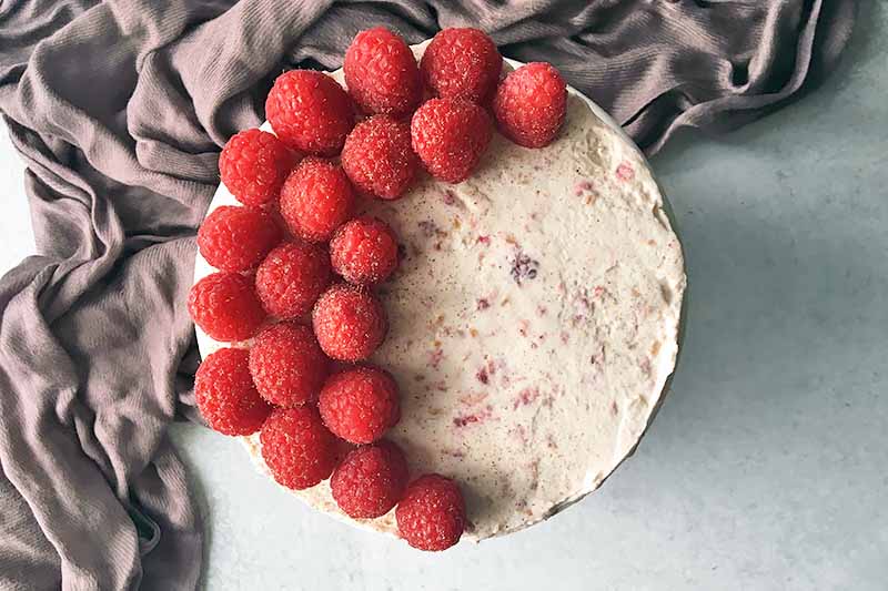 Horizontal top-down image of a cake garnished with fresh whole raspberries.