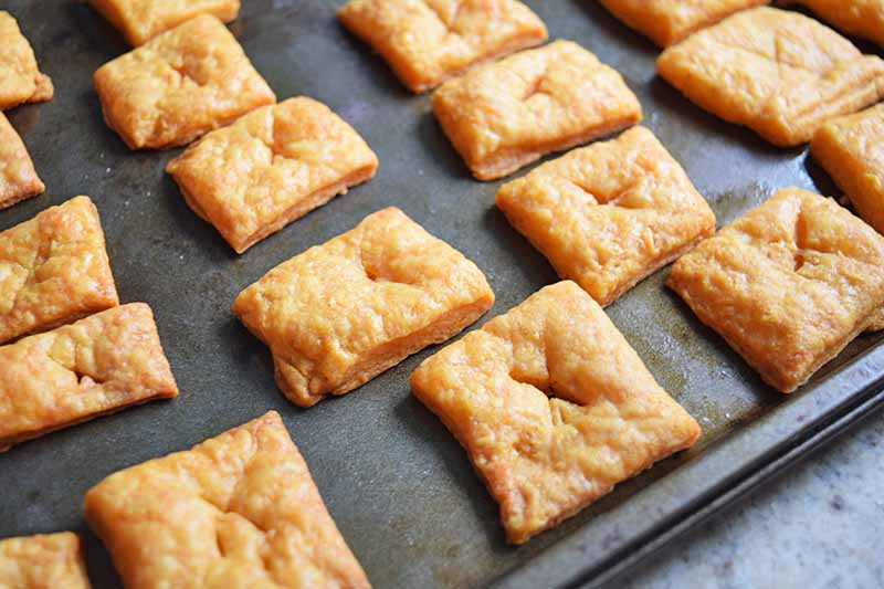 Closeup of square cheese crackers arranged in rows on a metal baking sheet.