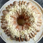 Horizontal image of a whole bundt cake with white glaze and white garnishes on a plate on a black surface.