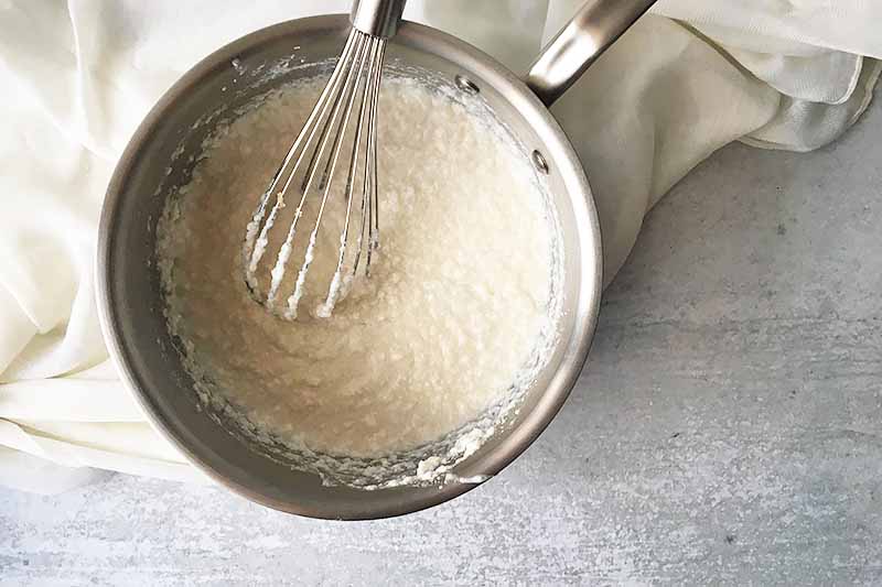 Horizontal image of a pot with a lumpy white batter and a whisk on top of a white towel.
