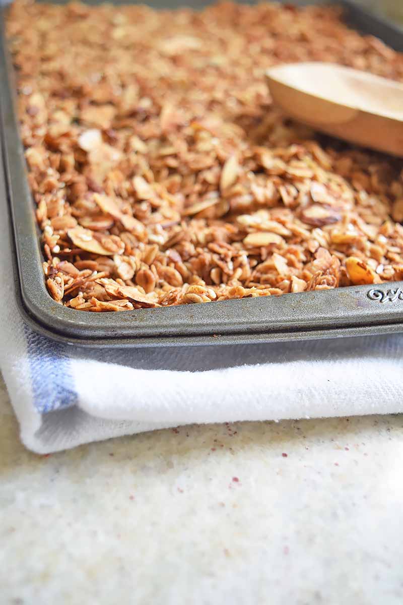 Vertical image of a baking sheet pan filled with baked granola on a white towel.