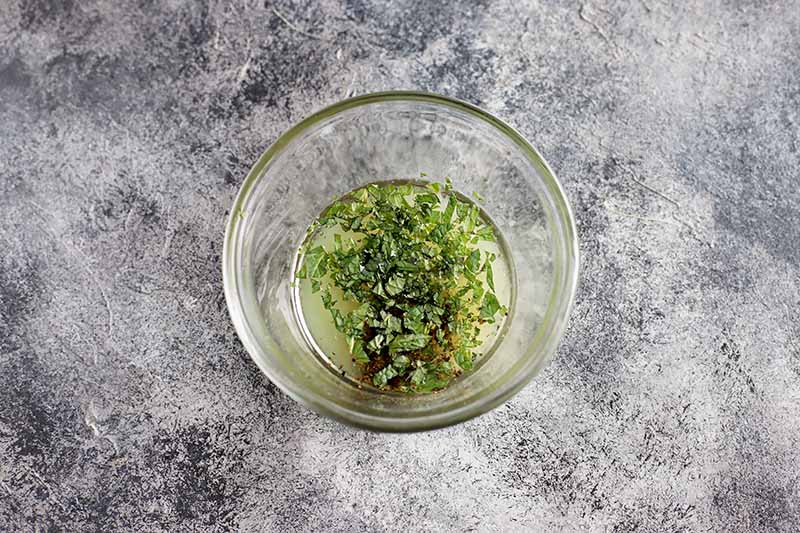 Horizontal image of a glass dish with fresh herbs and liquid.