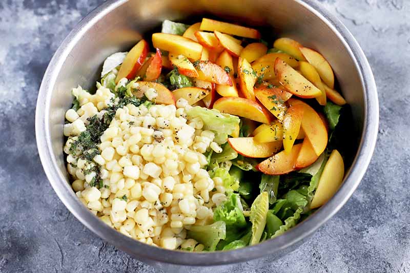Horizontal image of a large bowl with a pile of fresh peaches and corn on top of lettuce.
