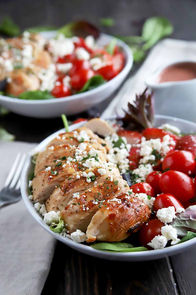 Vertical image of two salad plates with sliced chicken, cheese, and whole grape tomatoes.