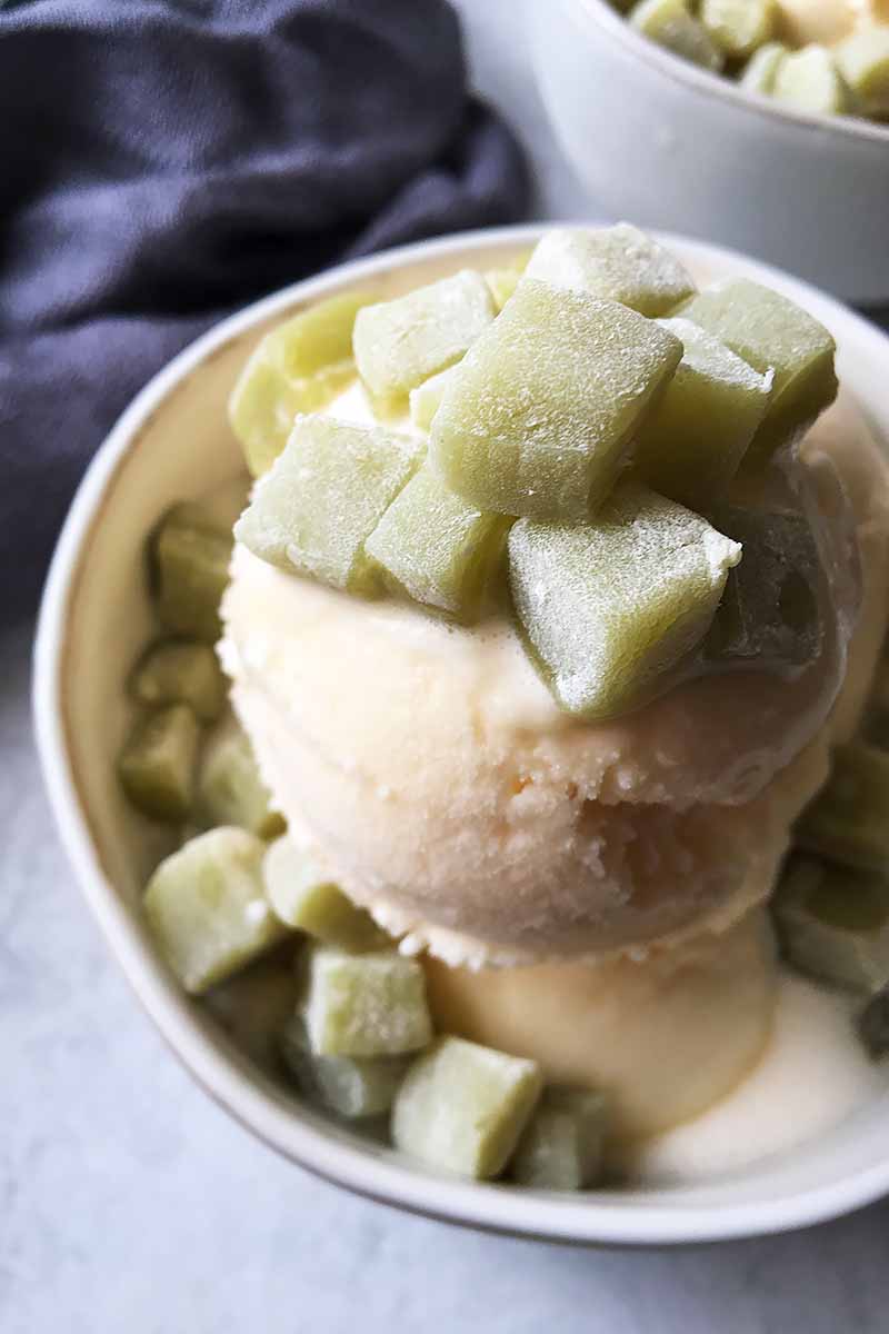 Vertical image of an ice cream dish topped with green squares of mochi, with a gray napkin in the background.