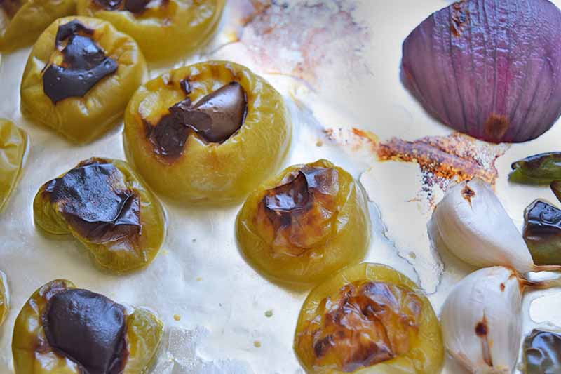 Charred tomatillos, red onion, and garlic, on a foil-covered pan.