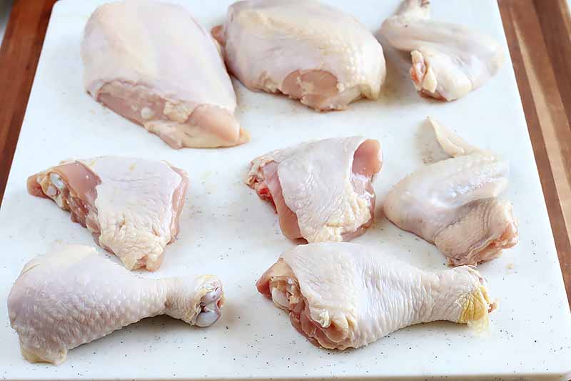 Horizontal image of a broken down raw chicken in all the main pieces.