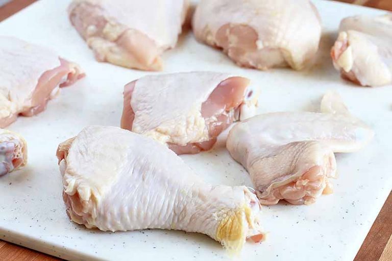 Horizontal image of the main parts of a raw chicken on a white cutting board.