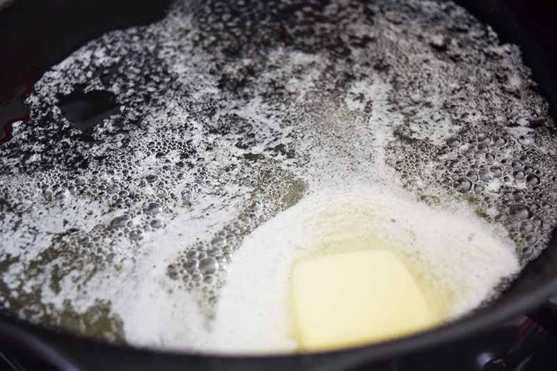 Vertical closeup image of melting and foamy butter in a large frying pan.