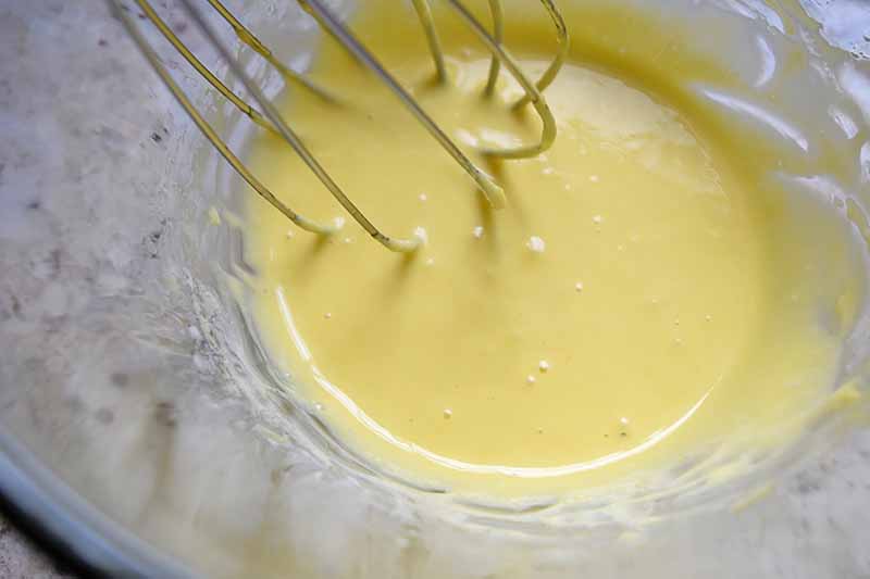 Closeup overhead horizontal image of a yellow mixture being whisked in a mixing bowl.
