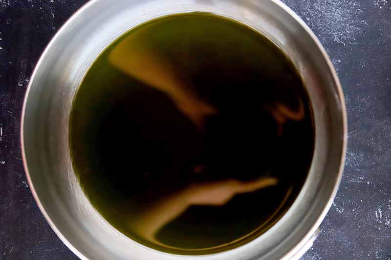 Green flavored olive oil in a stainless steel mixing bowl, on a gray slate surface.