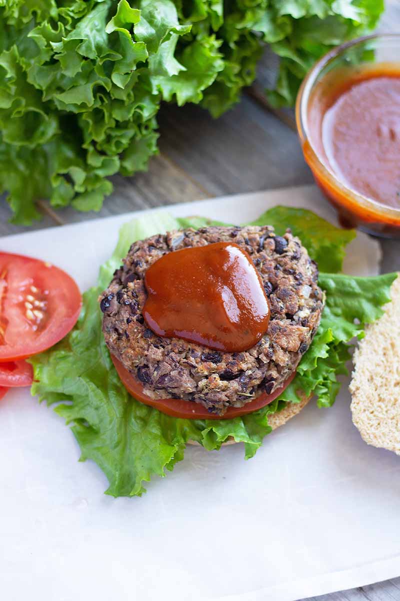 Vertical image of an open-faced bean burger on top of tomato, lettuce, and a bun and topped with ketchup.