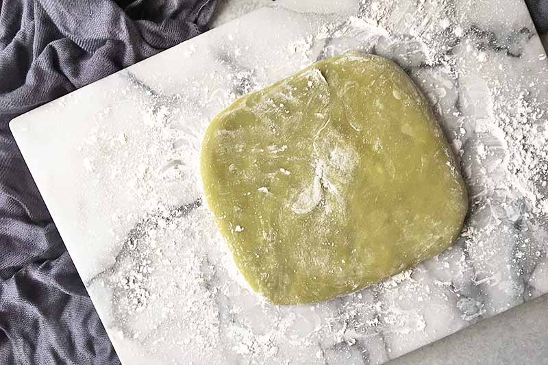 Horizontal image of a green dough on a marble board dusted with cornstarch.