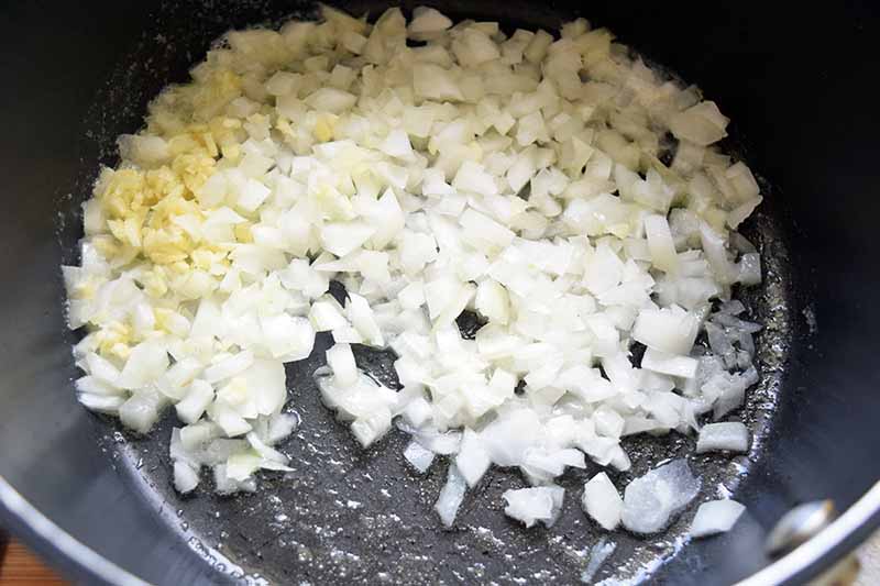 Overhead horizontal image of chopped white onion and minced garlic in a nonstick frying pan.