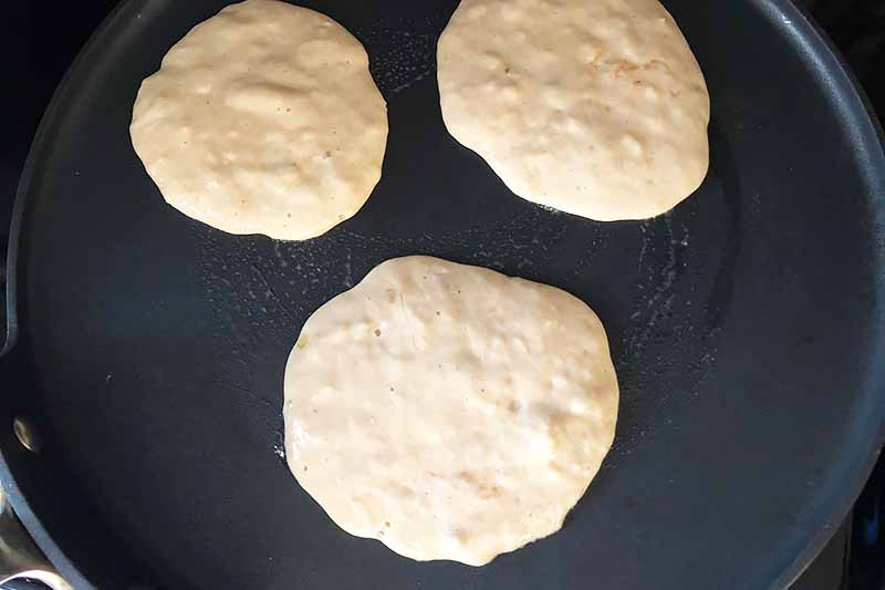 Horizontal image of a pan with three uncooked flapjacks.