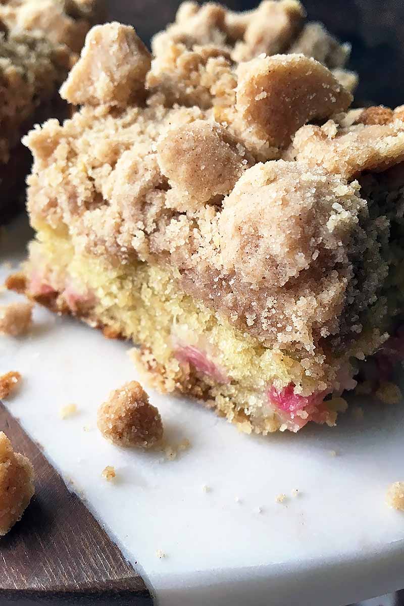 Vertical image of a piece of rhubarb coffee cake on a white surface.