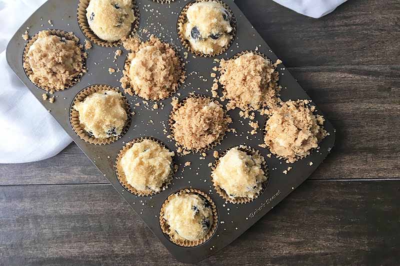 Horizontal image of a baking tin with muffin batter and crumb topping.