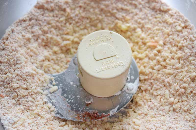 Horizontal closeup overhead image of a grainy flour mixture in a food processor.