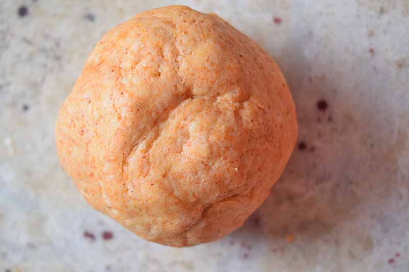 Horizontal overhead image of an orange ball of dough on a gray speckled countertop.