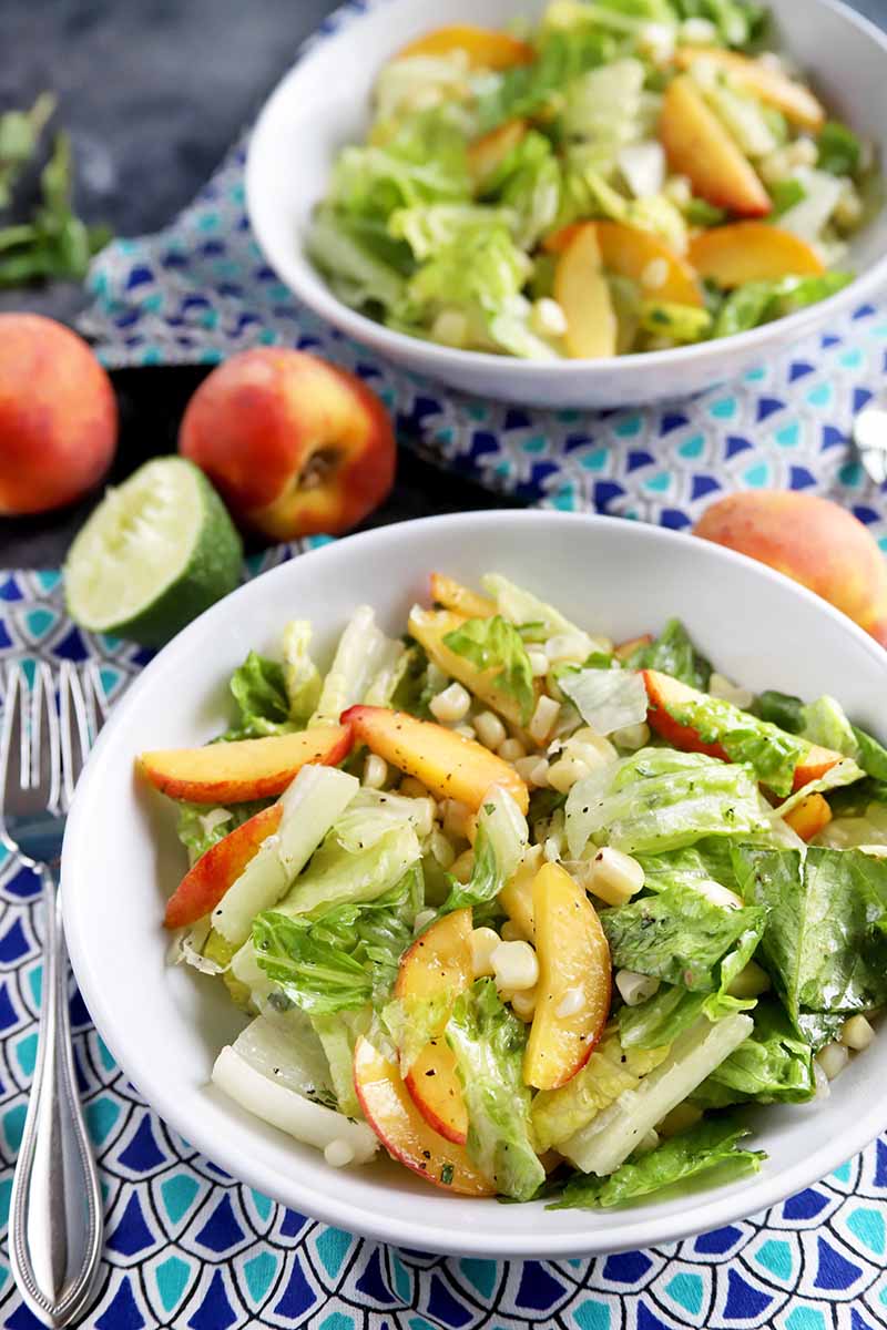 Vertical image of two white bowls filled with a fruit and veggie tossed salad on top of bright blue napkins.