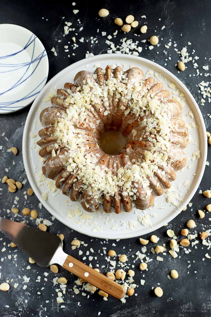 Vertical top-down image of a whole bundt dessert on a white plate surrounded by other empty plates and garnishes.