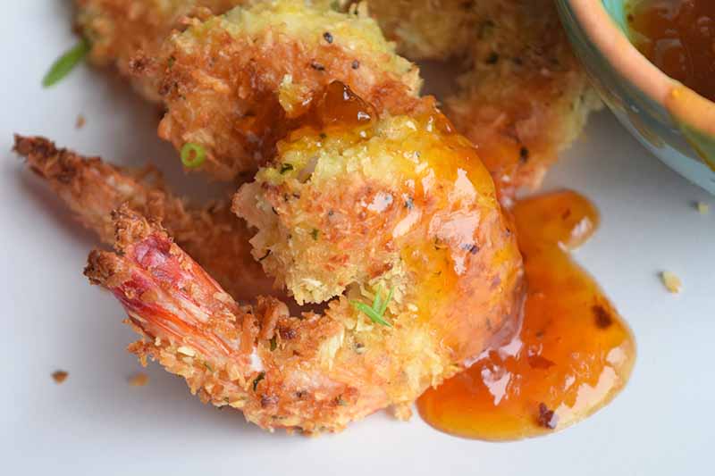 Horizontal closeup image of several baked coconut shrimp with sweet and sour sauce.